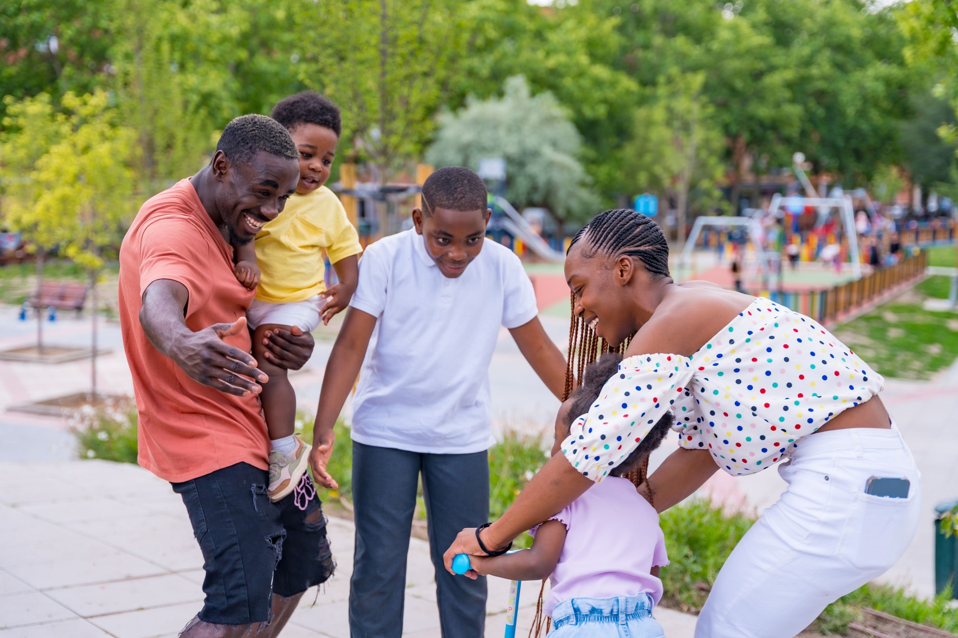 African black ethnic family with children in playground, hugging with bicycle
